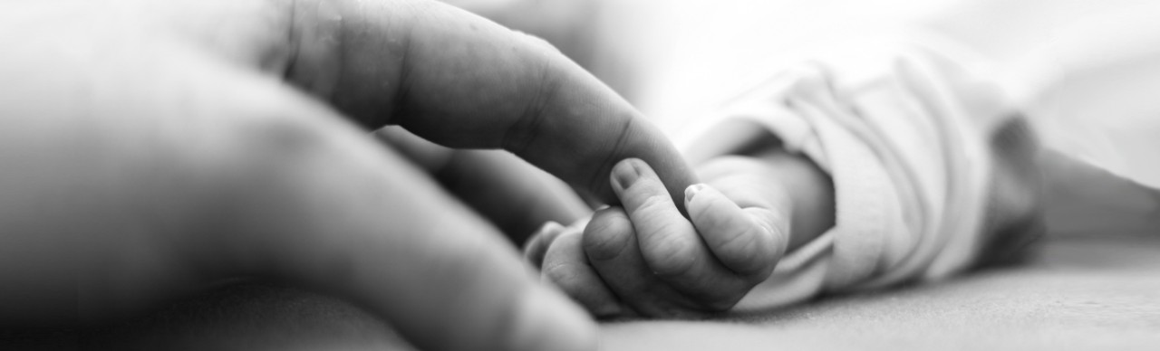 woman's hand holds newborn infant hand